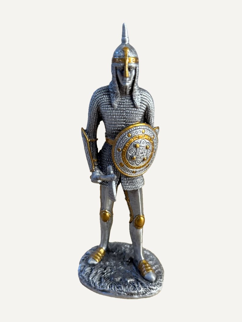 Pewter figurine of a warrior in mail with a pointed helmet and gold-tone nose guard, decorated round shield with gold-tone studs, sword in his right hand