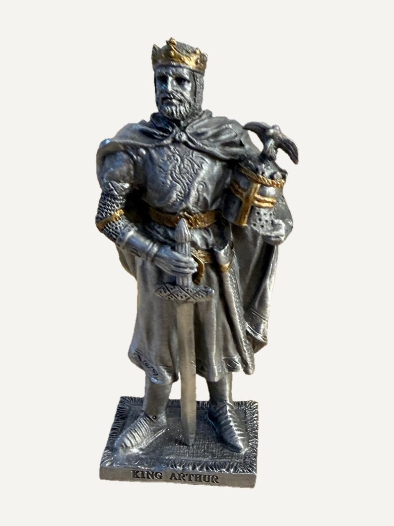 Statuetta in peltro di Re Artù: corona color oro, mantello, la mano destra su una spada con la punta in giù, sotto il braccio sinistro un elmo con un uccello sulla cima, scritta KING ARTHUR sulla base