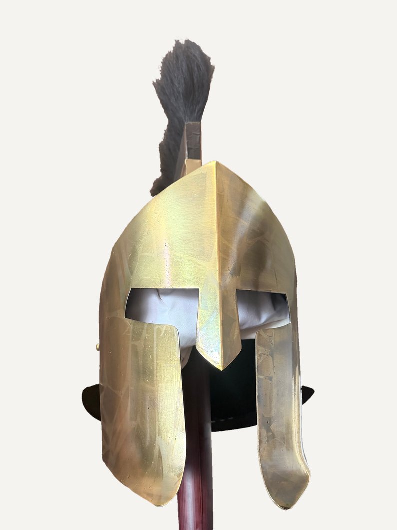 Leonidas Spartan helmet seen from the front: bronze-finish Corinthian-style helmet with eye openings, nose guard and long cheek guards, tall black crest, on the pole of a wooden stand