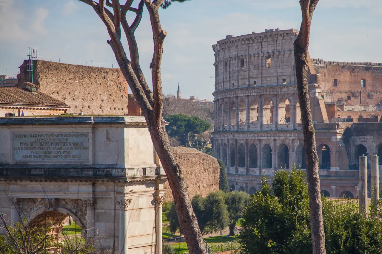 The attic of the Arch of Titus and, behind it, the Colosseum among the pines.