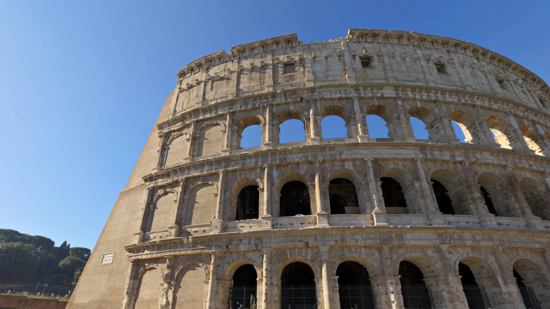 The Colosseum from the east side, photograph: the outer travertine ring with its arches and the lawn in front.