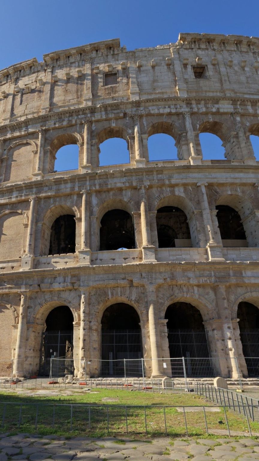 The Colosseum from the east side, photograph: the outer travertine ring with its arches and the lawn in front.
