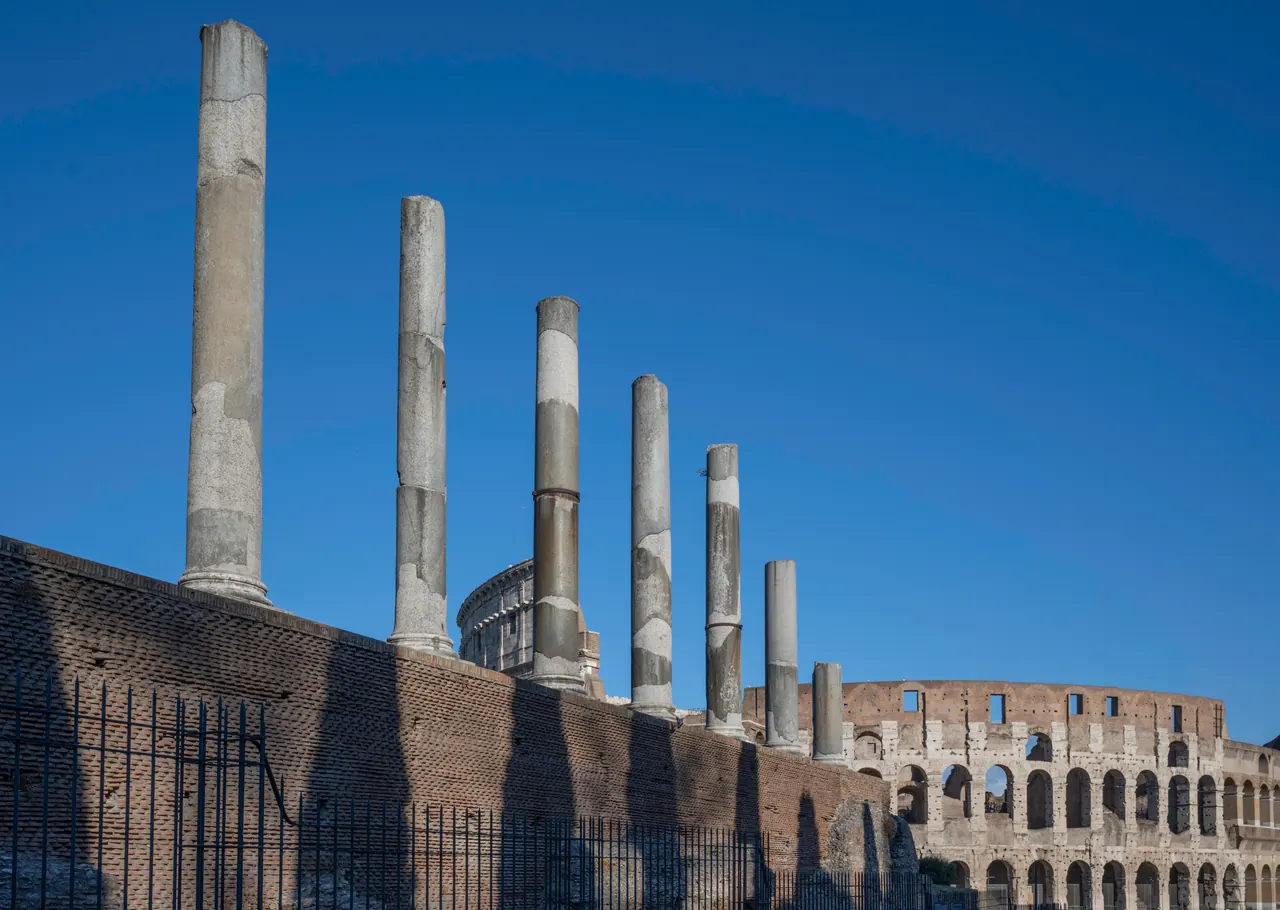 Columns of the Temple of Venus and Roma against the sky, with the Colosseum behind.